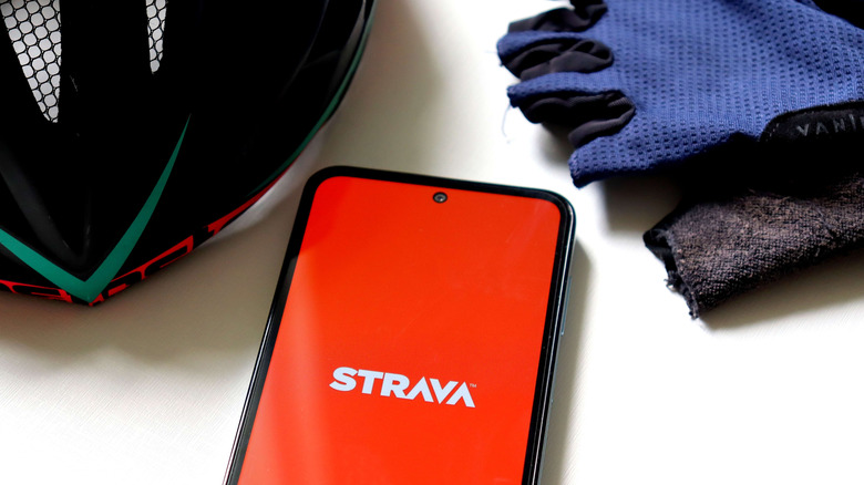 Strava app open on a smartphone. A bicycle helmet and gloves sit near it
