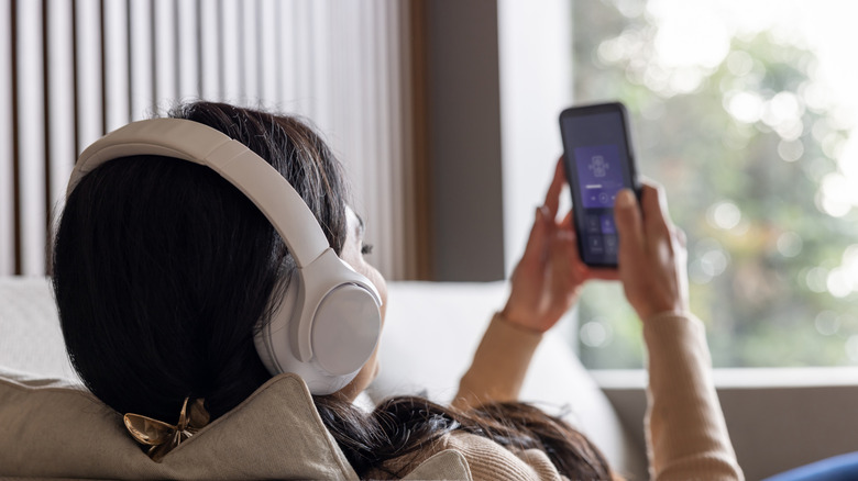 A person leaned back on a couch wearing headphones and looking at their phone