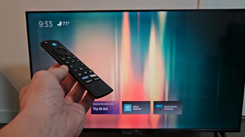Hand holding remote of Amazon Fire TV Stick in front of TV showing Ambient Experience