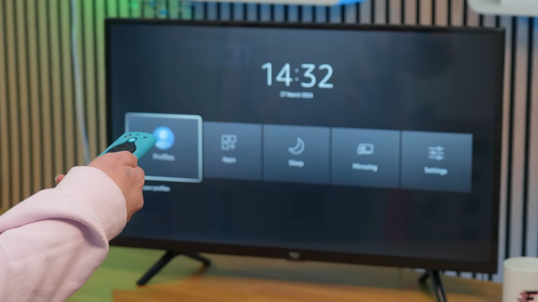 Hand holding Amazon Fire TV remote with TV showing secret shortcut