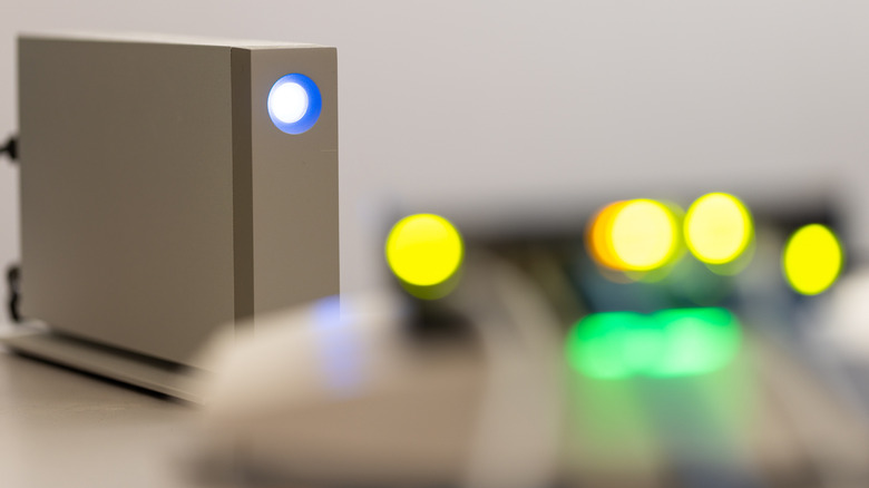 An external drive with light on and network lights blurred in foreground.