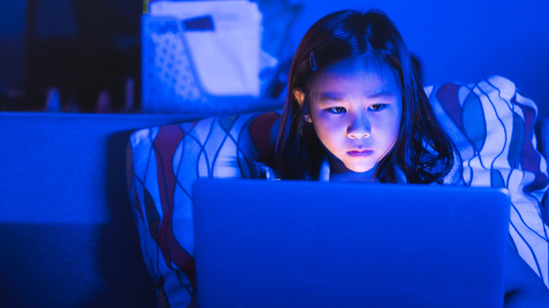 Young girl using her laptop in the evening with screen glow visible.