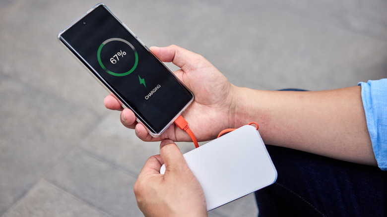 A person holding a phone that is being charged by a power bank