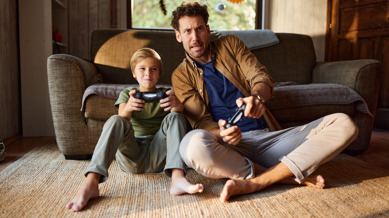 A man and a boy sitting on the floor holding controllers playing games