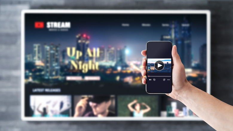 A hand holding a phone up to a TV, streaming content from it