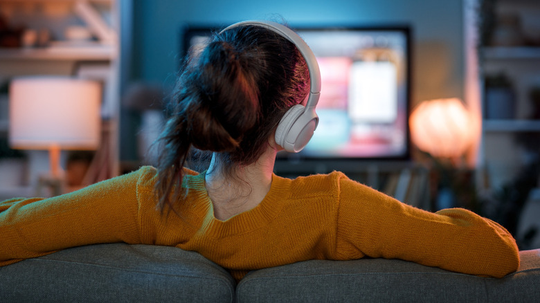 A woman wearing headphones while watching TV