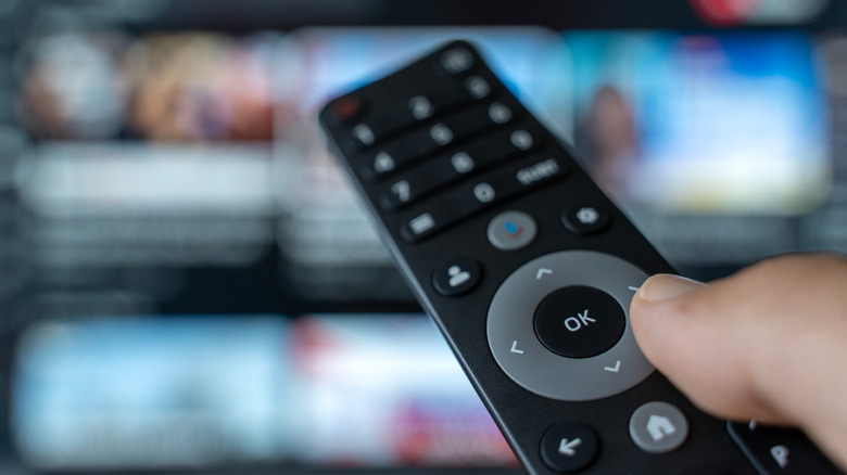 Hand holding a TV remote with blurred streaming interface in background