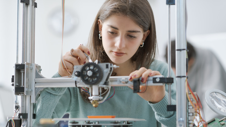 Woman adjusting components on a desktop 3D printer