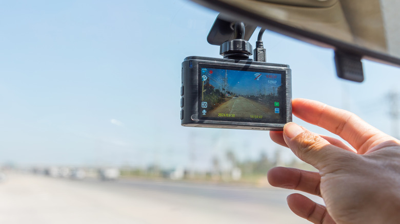 A person adjusting a dash cam attached behind a rearview mirror