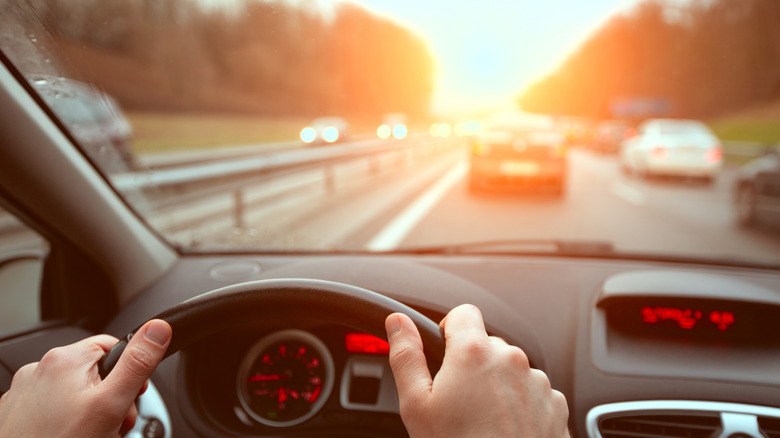 A person driving a car. We don't see them, but we do see their hands on the steering wheel.