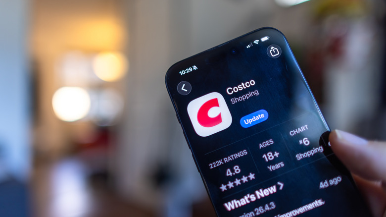 A closeup of the Costco app within the Apple App Store as it is being displayed on an iPhone, the device is behind held in a user's right hand, though the background is extremely blurred