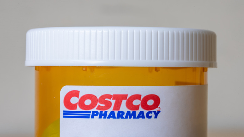 A closeup of a pill bottle displaying the Costco Pharmacy logo, the background is a plain grey