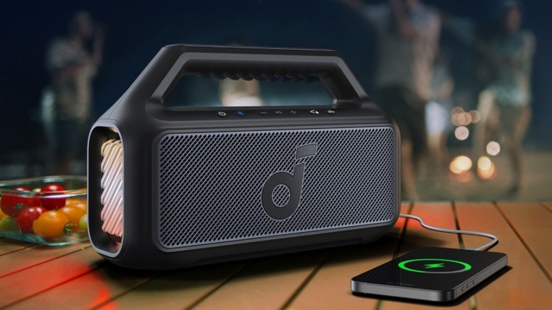 The Soundcore Boom V2 Bluetooth Speaker on a wooden surface, playing music while charging a smartphone.