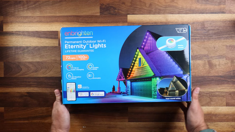 A pair of hands prepare to open a bright blue, Enbrighten Eternity Lights kit upon a wood table.