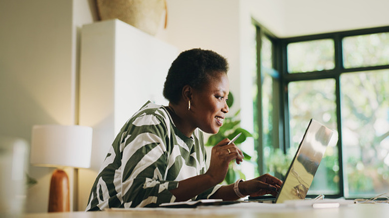 A woman leans in and smiles as she scours the internet on her laptop in the center of a well lit office.