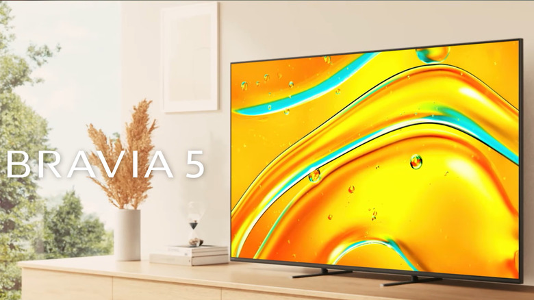 A Bravia 5 television shows off its high definition display with a bright image of sun kissed water droplets atop a flower-ornamented dresser.