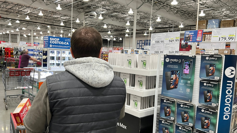 Customer walking through the electronics section inside a Costco warehouse, with smartphones on display