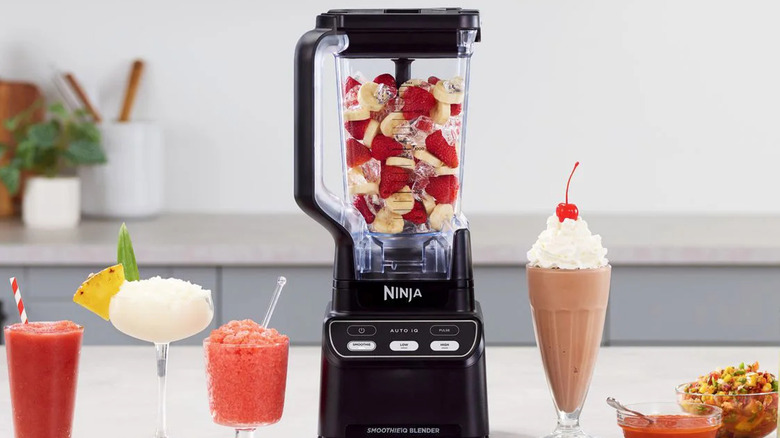 A Ninja Professional Blender filled with fruits and ice, next to smoothies and shakes on a countertop