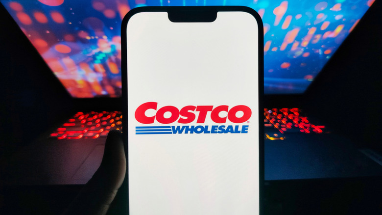 The Costco logo on a phone with a laptop in the background