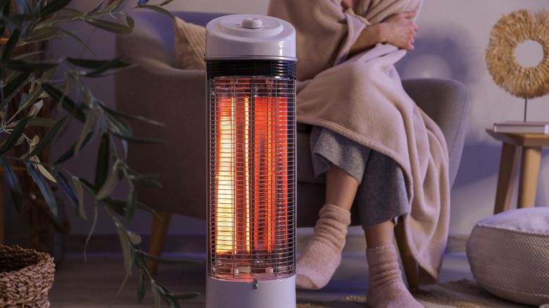 A portable heater with a woman wrapped in a blanket in the background