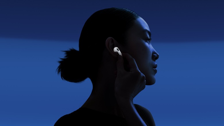 An individual immersed in dark blue light places a white Apple AirPods 4 ear pod to their ear