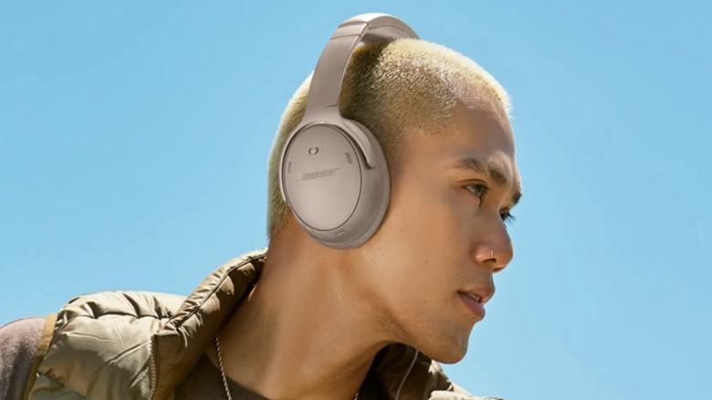 A young person with a shaved blonde head is wearing a pair of Bose QuietComfort SC Noise Cancelling Headphones