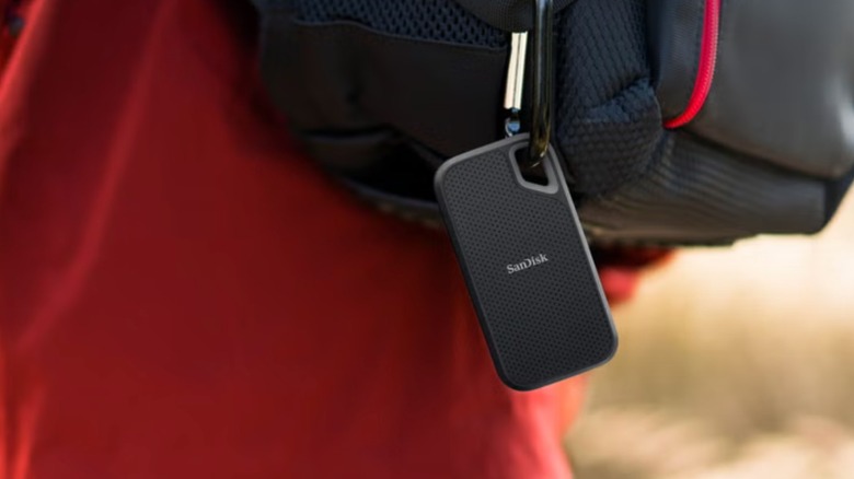 A closeup of a SanDisk Extreme Go 2TB Portable SSD attached to a black backpack being worn on an individual