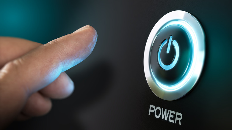 A finger inching closer to an illuminated power button to turn of nondescript device.