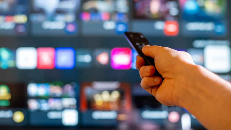 Someone holding up a remote with a smart TV interface blurred in the background.