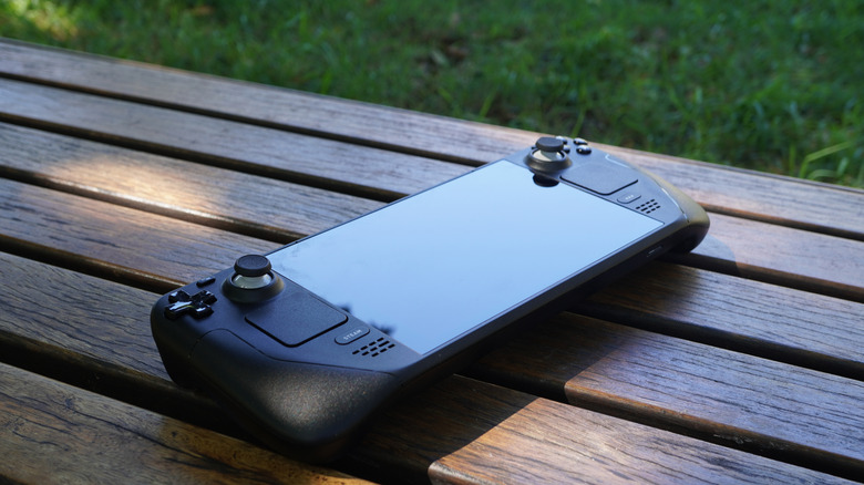 Image of a Steam Deck with no case resting atop a wooden table outdoors.