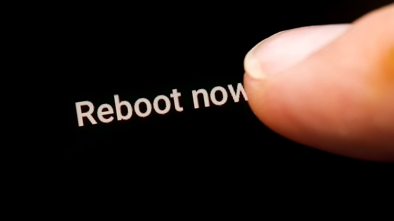 Close up of someone pressing a "reboot now" option on a smartphone display.
