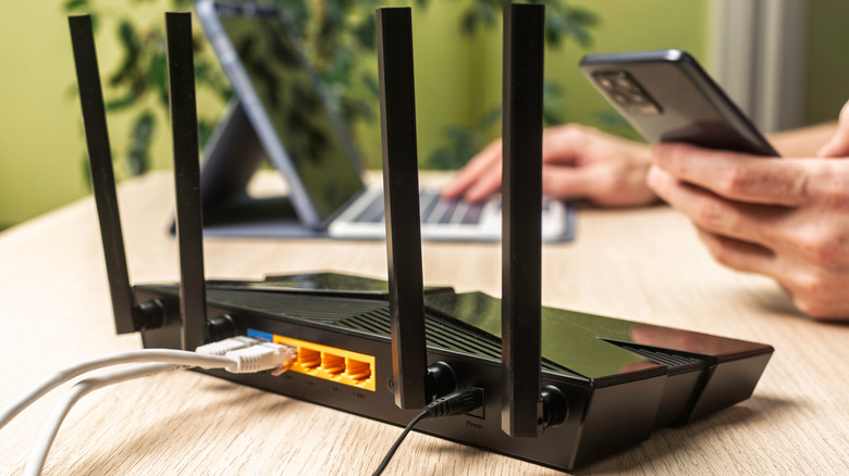 A wireless router with four antennas being tested by a person using a phone and laptop to run diagnostics.