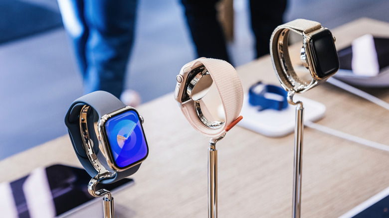 : In the backdrop of bustling customers inside an Apple Store, a trio of watches from the Watch 9 and Ultra 2 lineup are actively charging on display
