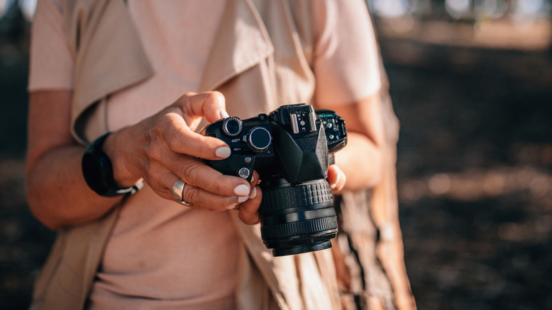 Close-up of fashionable mature female photographer using DSLR camera outdoors during summer holidays