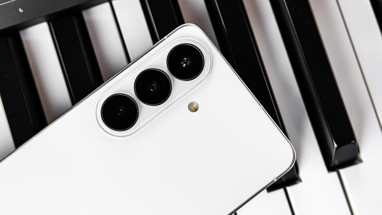A white Android devices sits on top of a row of piano keys