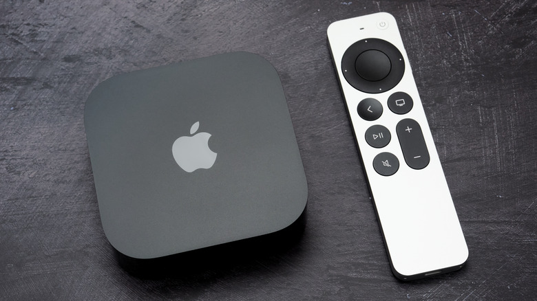 A black Apple TV 4K sits on a black surface next to its silver Apple TV Remote