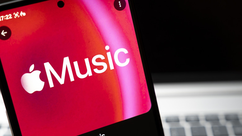 An iPhone displaying the Apple Music logo as it sits in front of a heavily blurred MacBook in the foreground