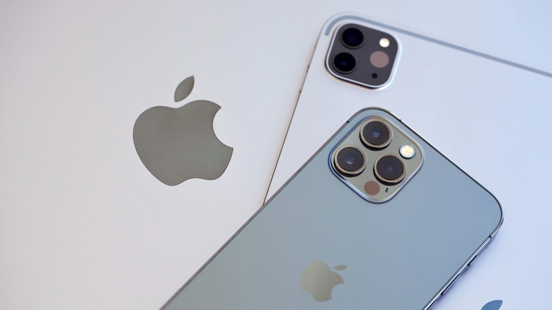 A silver iPad and a black iPhone sit on top of what is likely a MacBook, though the photo is cropped that only the MacBook's Apple logo can be seen