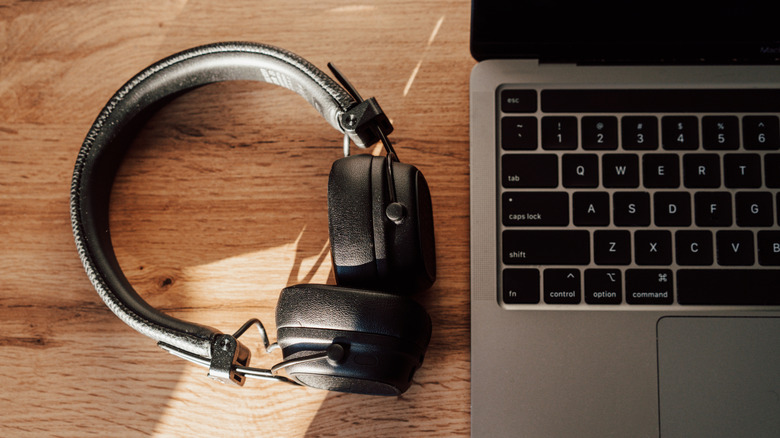 A pair of black over-ear headphones sit next to a black MacBook, both objects are on a wooden surface