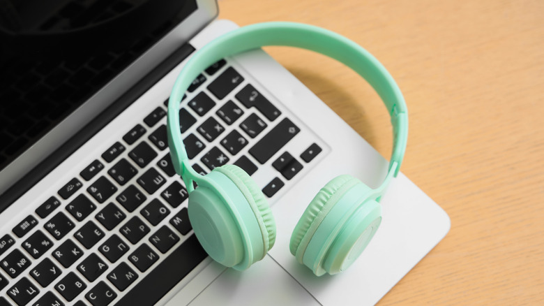 A pair of emerald-colored headphones sit on top of a silver laptop that has black keys