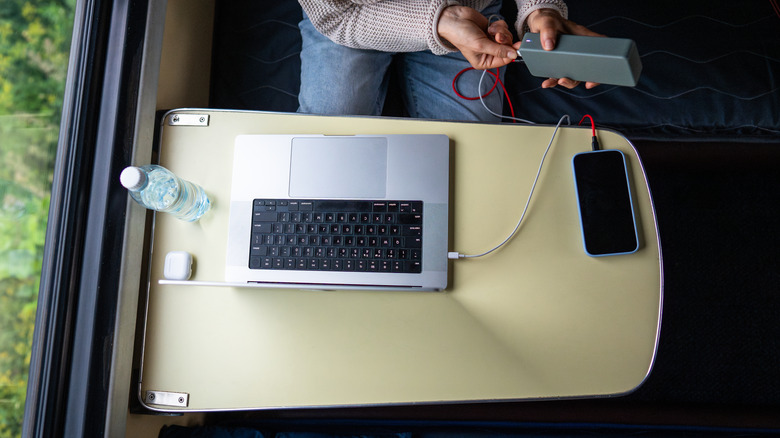 A person charging a phone and laptop from a power bank in a train