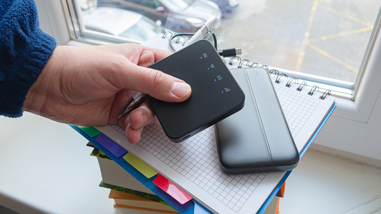 man holding a portable router next to a power bank placed on a stack of books