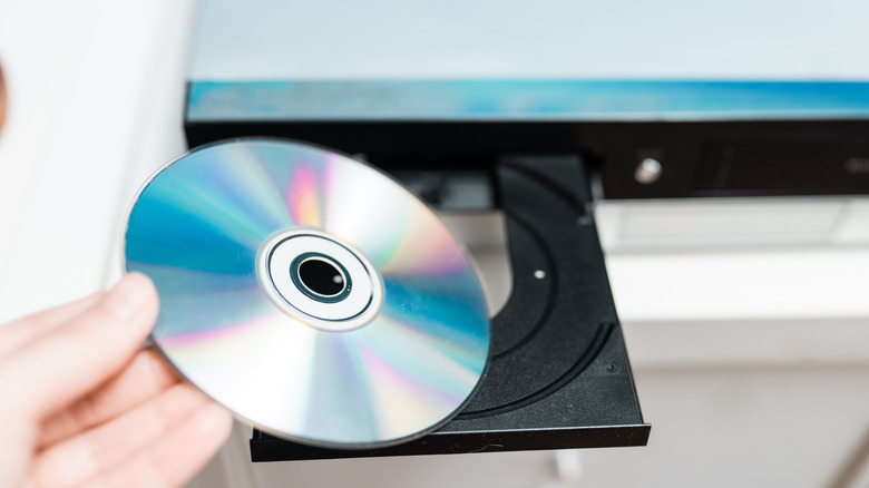 A person holding a disc in front of a Blu-ray player with its disc tray ejected.