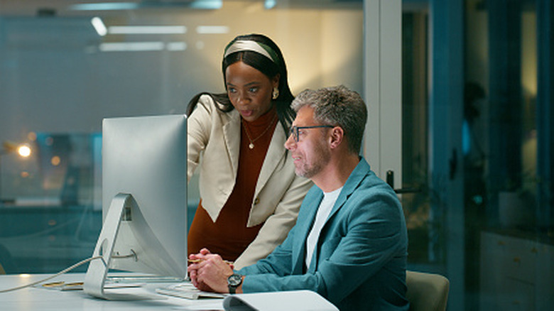 A man and woman huddled around a computer in an office setting.