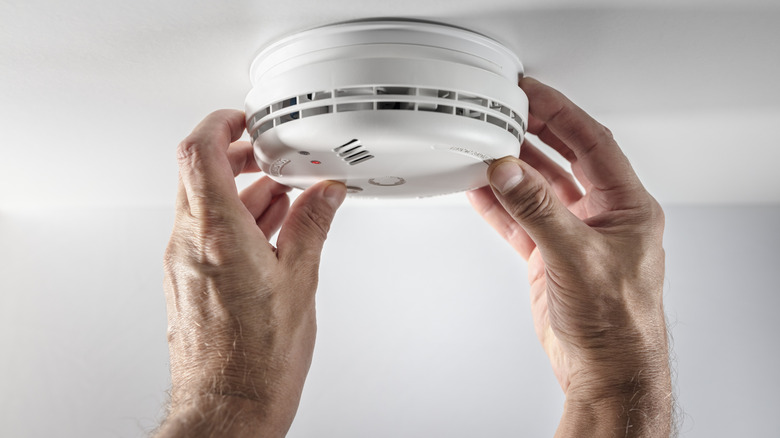 A person inspecting a smoke and fire alarm inside a house
