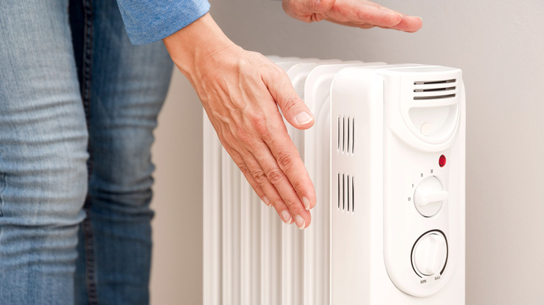 A person holding their hands over an electric radiator.
