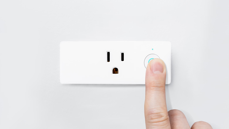 A person powering on a smart plug.