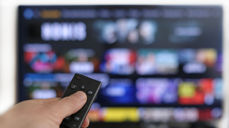 A person holds a remote control in front of  blurred smart TV screen