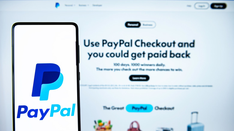 The PayPal logo displayed on a smartphone in front of a webpage marketing PayPal Checkout