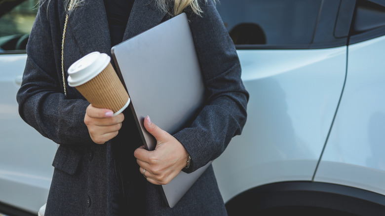 A woman holding a large laptop and a cup of coffee.